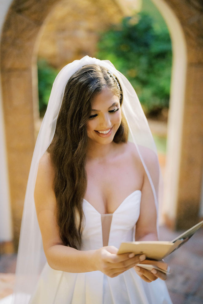 A bride with a deep v-neck wedding gown and long veil reads a card from her groom..