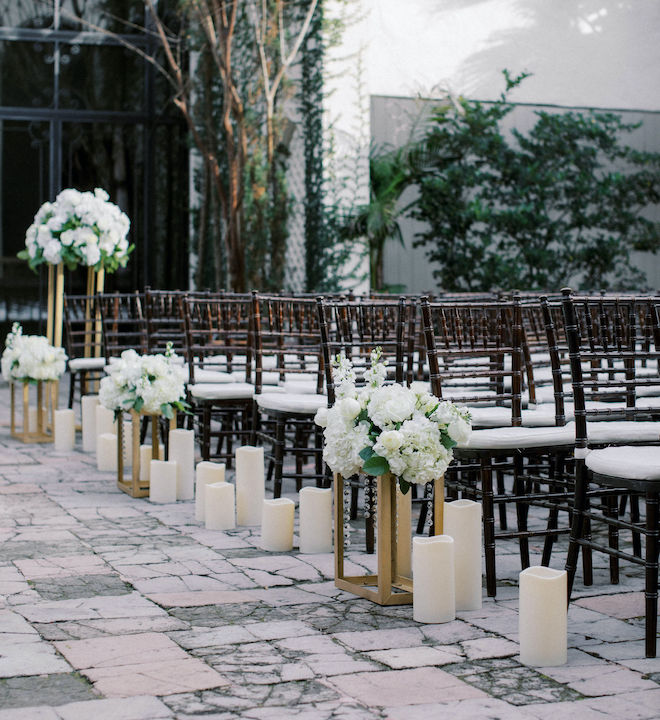 White floral installations, pillar candles and chiavari chairs decorate a courtyard at a Houston wedding venue. 