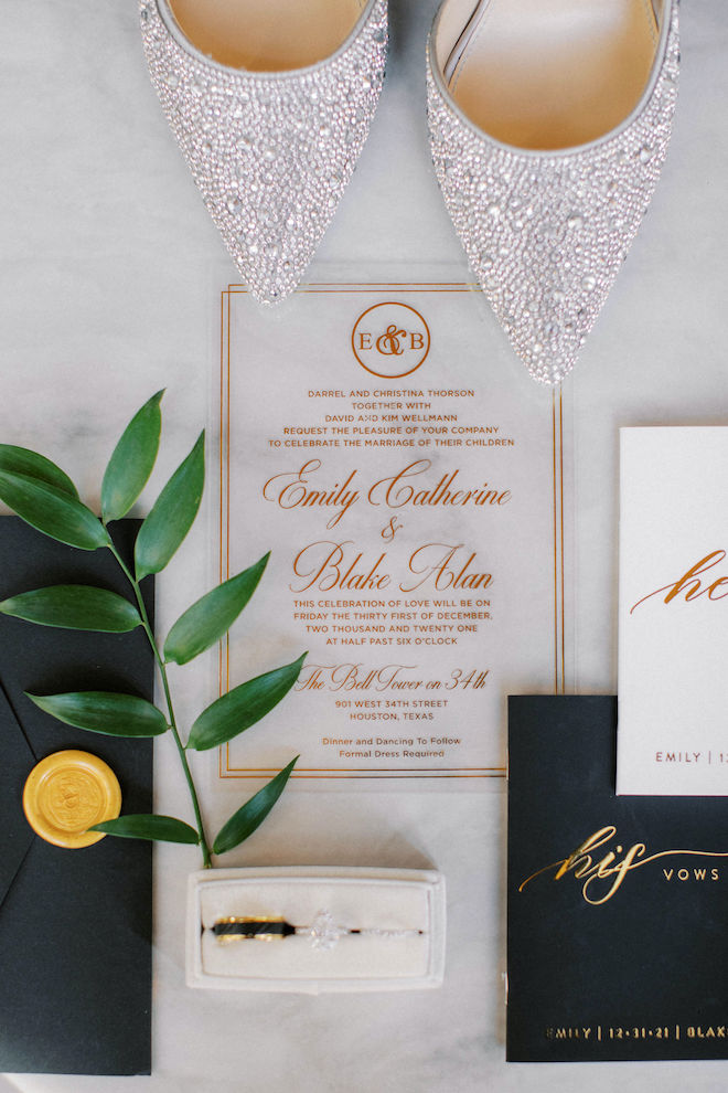 Acrylic wedding invitation with gold script, black envelope with gold seal, notebooks that read "His vows" and "Her Vows" 