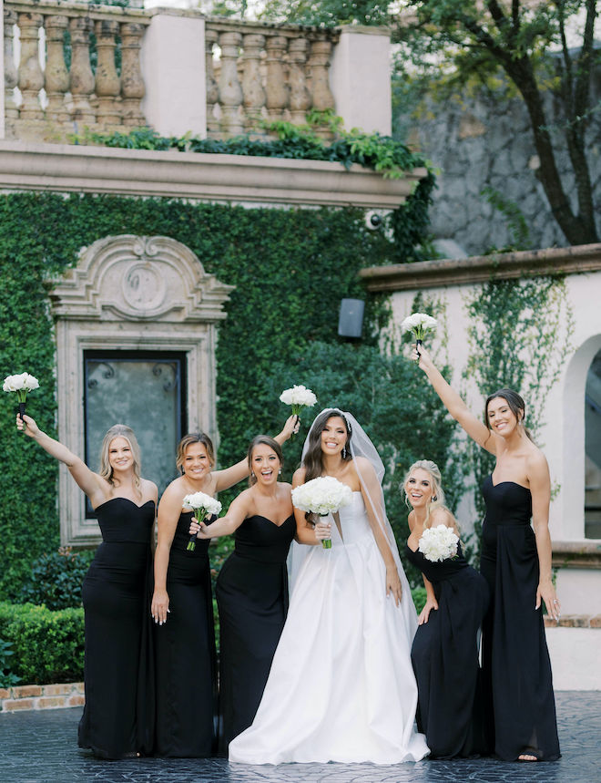 Bride and bridesmaids smile and hold white bouquets outside of wedding venue, The Bell Tower on 34th. 