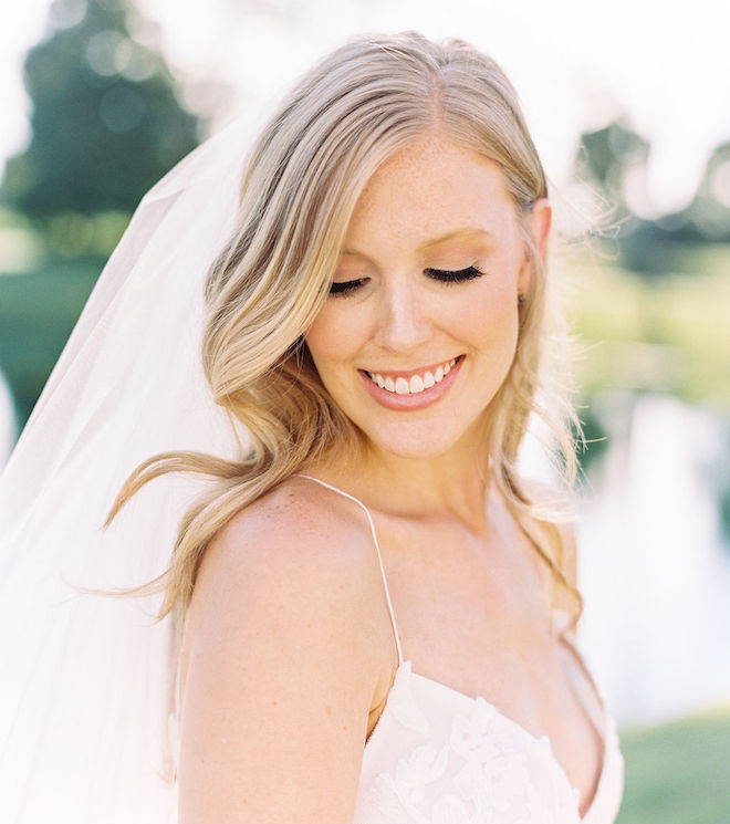 The bride looking down and smiling in her Monique Lhuillier dress.