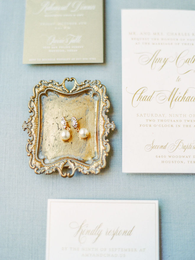 Ivory and gold wedding invitation suite and pearl drop earrings in a gold tray.
