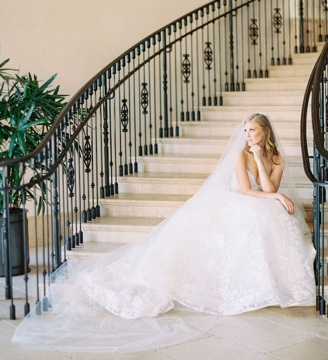 The bride looking to the side as she sits on a grand stairway. 