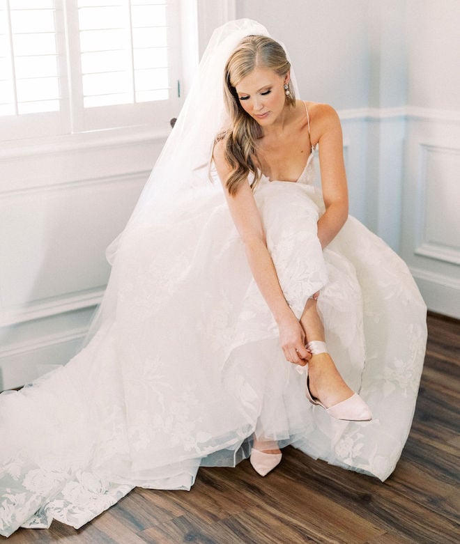 A bride putting on blush flats before her Houston wedding ceremony.