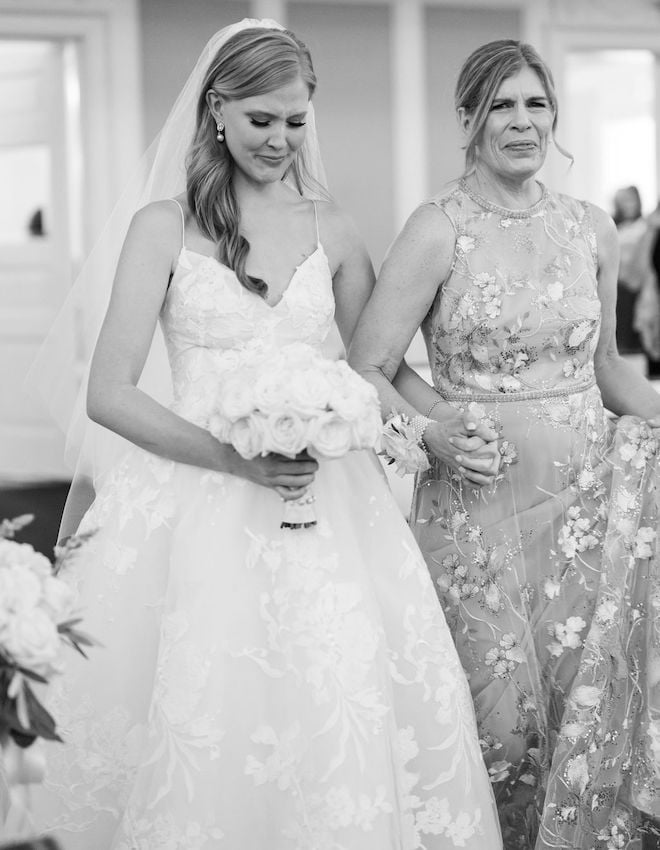 The bride holding hands with her mother, emotional as they walk down the aisle.