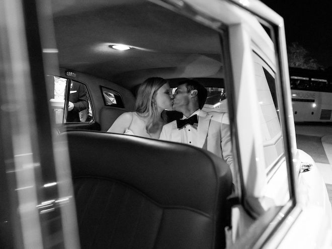 The bride and groom kissing as they drive away in a vintage Rolls Royce. 