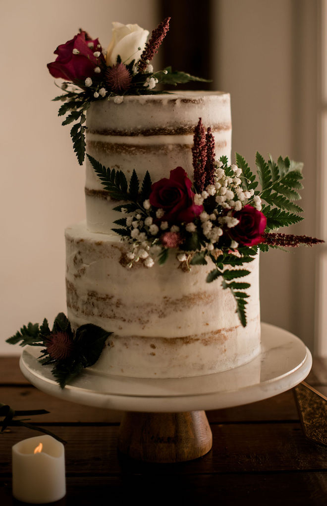 Two-tiered rustic chic white wedding cake garnished with red roses.