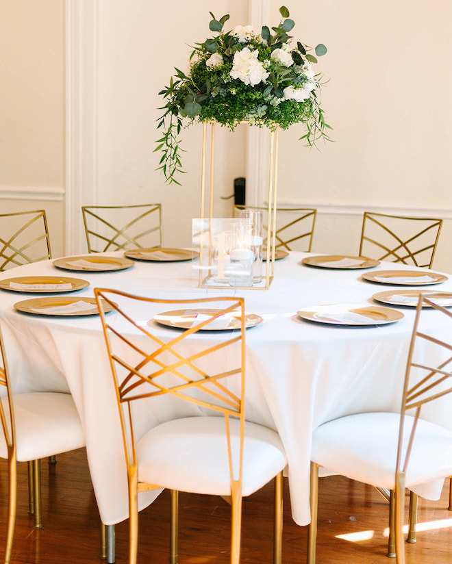 Contemporary gold chairs and table accents with a white floral and greenery centerpiece at this traditional wedding reception.