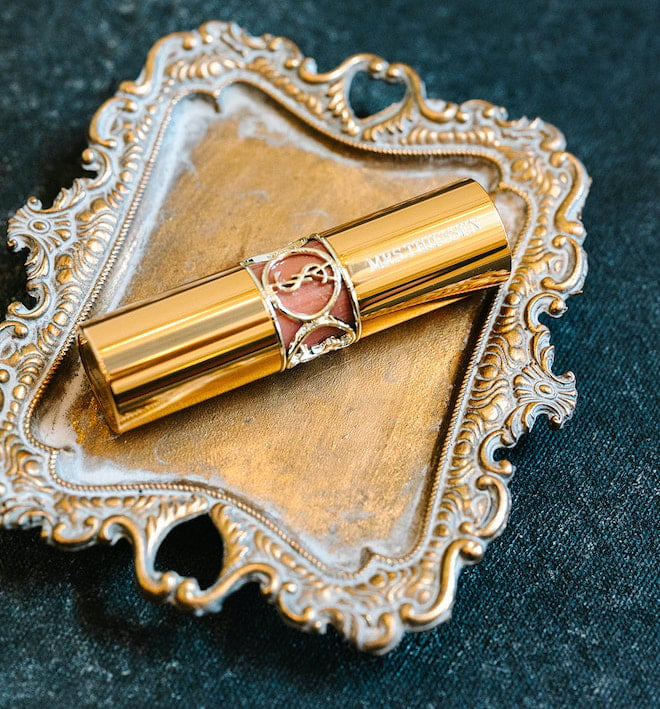 A gold tube of lipstick laying on a gold tray.