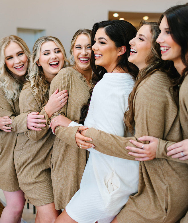 The bride laughing with her bridesmaids as they all hug around her.