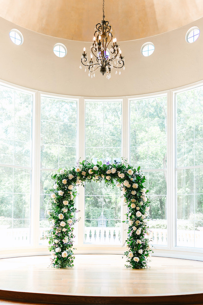 The altar covered in green and white florals behind grand windows.