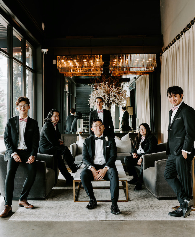 Groom and groomsmen, in black suits and blush ties, posing in the ground level foyer of the Astorian.
