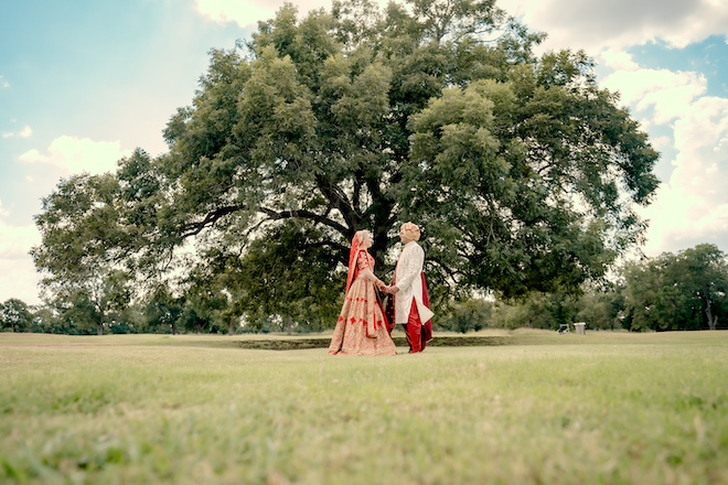 The bride and groom hold hands under an oak tree at the wedding venue, The Hyatt Regency Lost Pines Resort and Spa.