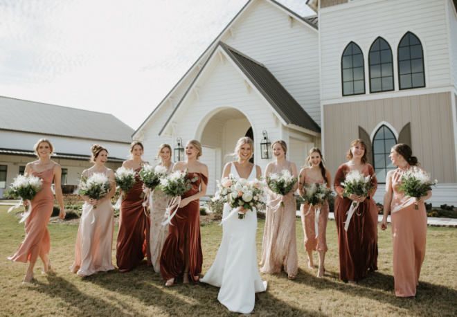 The bride and her bridesmaids walk outside the wedding venue, Deep in the Heart Farms in Brenham, TX.