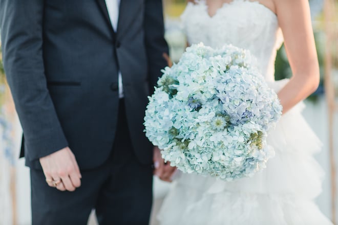 A detail of bride and groom holding hands and the brides hydrangea bouquet