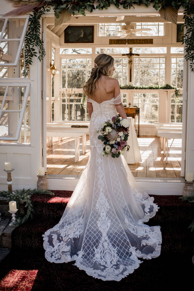 The back of the brides gown with a flower bouquet in her hand at the chapel.