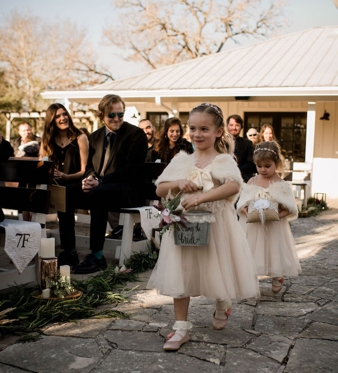The flower girls holding a tin bucket and burlap lace pillow walking down the aisle for the charming ceremony.