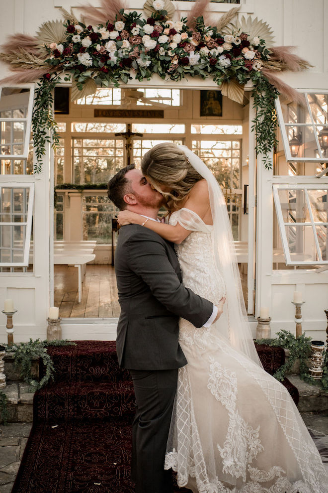 The bride and groom kissing in front of the floral-filled chapel.