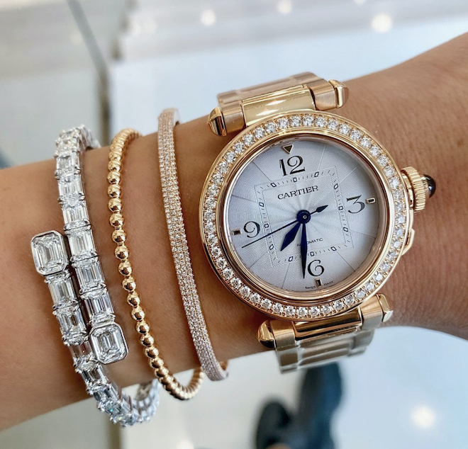 Woman's wrist with three gold and diamond bracelets and a gold Cartier watch.