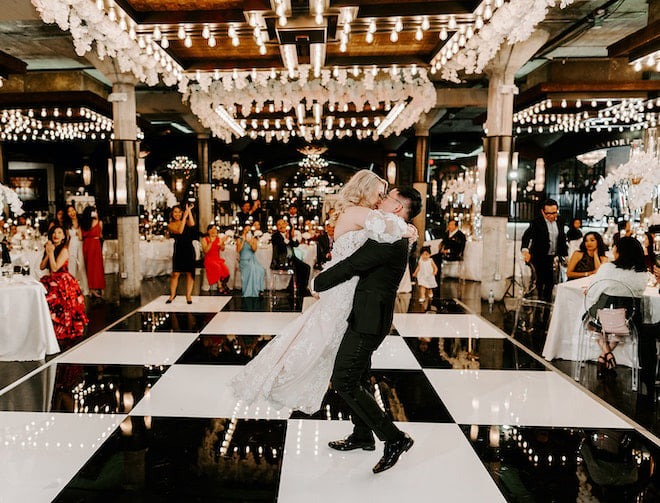 Bride and groom kiss on the dance floor while guests watch and clap at a wedding reception at wedding venue, The Astorian. 