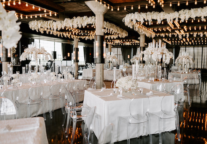 The white reception tables with clear chars, with glamorous white flowers dripping from the ceiling. 