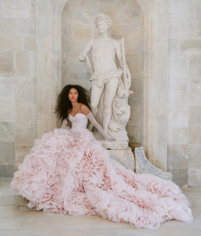 Monique Lhuillier model posing in front of a statue while wearing a pink gown with matching gloves.