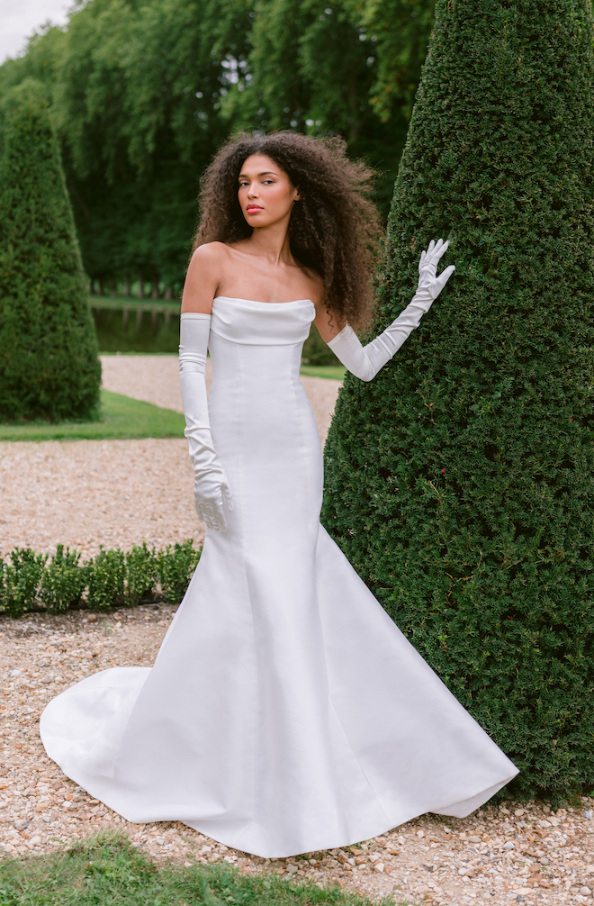 Model wearing a strapless satin wedding dress with matching gloves.