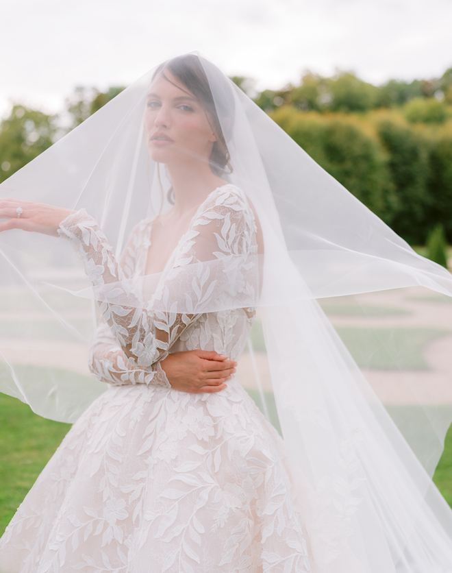 Detailed Monique Lhuillier gown worn by a model with a veil over her head.