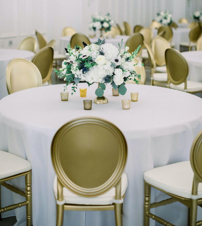 The white and blue floral centerpiece surrounded by small candles on white table linens.