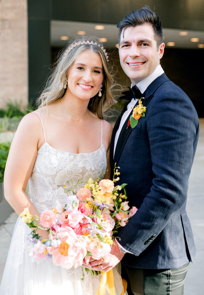 The bride and groom smiling with the bride holding her colorful bouquet. 