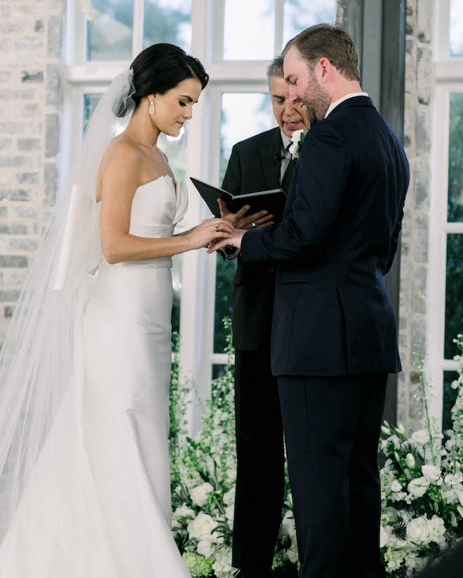 The bride putting the grooms ring on his hand during their ceremony at their fall wedding.