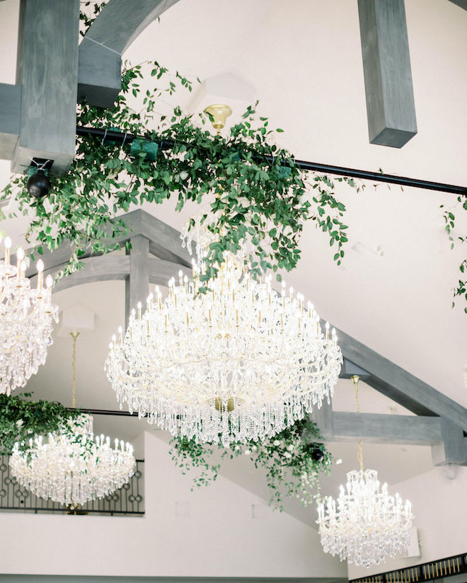 Chandeliers dripping with crystals intertwined with lush greenery hanging from the ceiling in the reception hall.