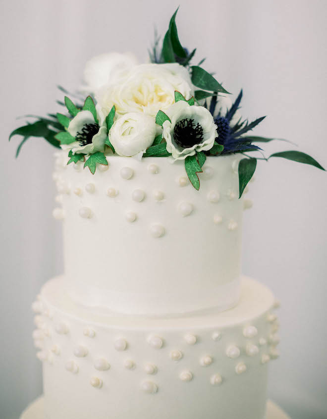 A grand four-tiered wedding cake topped with white and blue florals below. 