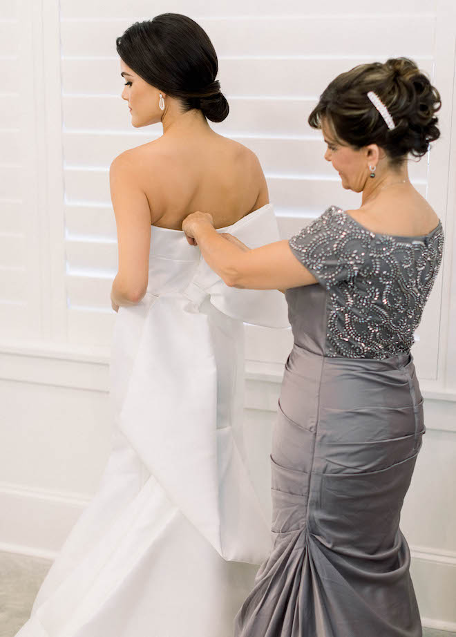 A woman adjusting the bow on the back of the bride's bright white wedding gown.