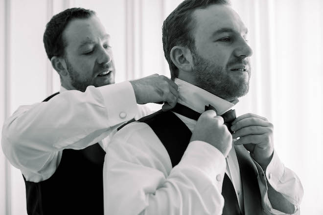 A groomsman assisting the groom with putting on his bowtie before the ceremony.