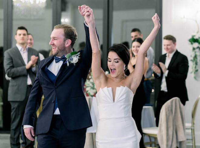 The couple walking into the reception while holding hands with their arms in the air. 