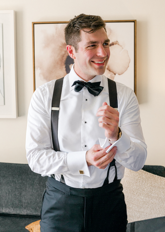 The groom smiling as he puts on his cufflinks before the wedding.