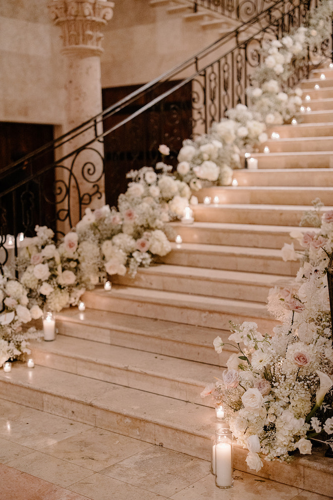 Staircase in the ballroom of venue, The Bell Tower on 34th, lined with lit candles, blush and white florals and greenery 