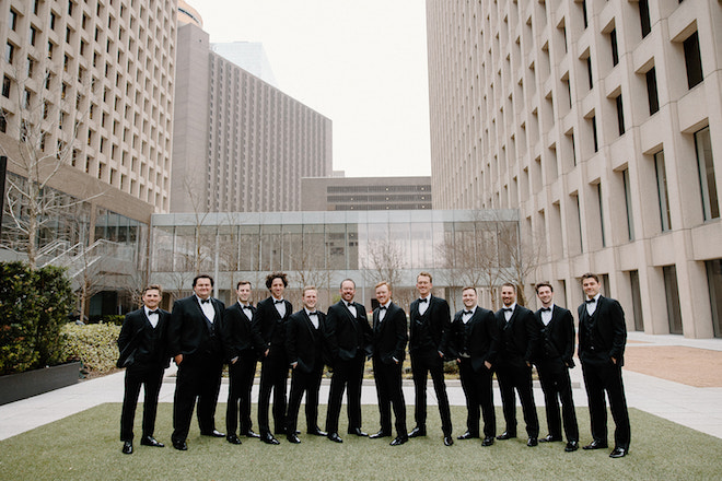 Groomsmen and groom wearing black suits stand on the lawn outside of Houston Hotel, C. Baldwin Hotel. 