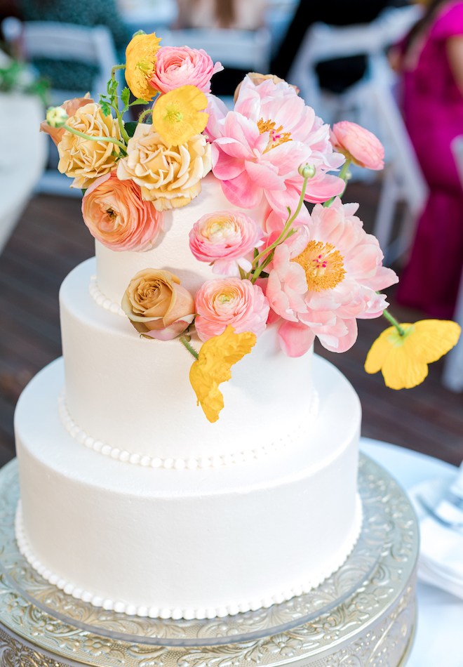 A three-tiered white cake garnished with colorful florals. 