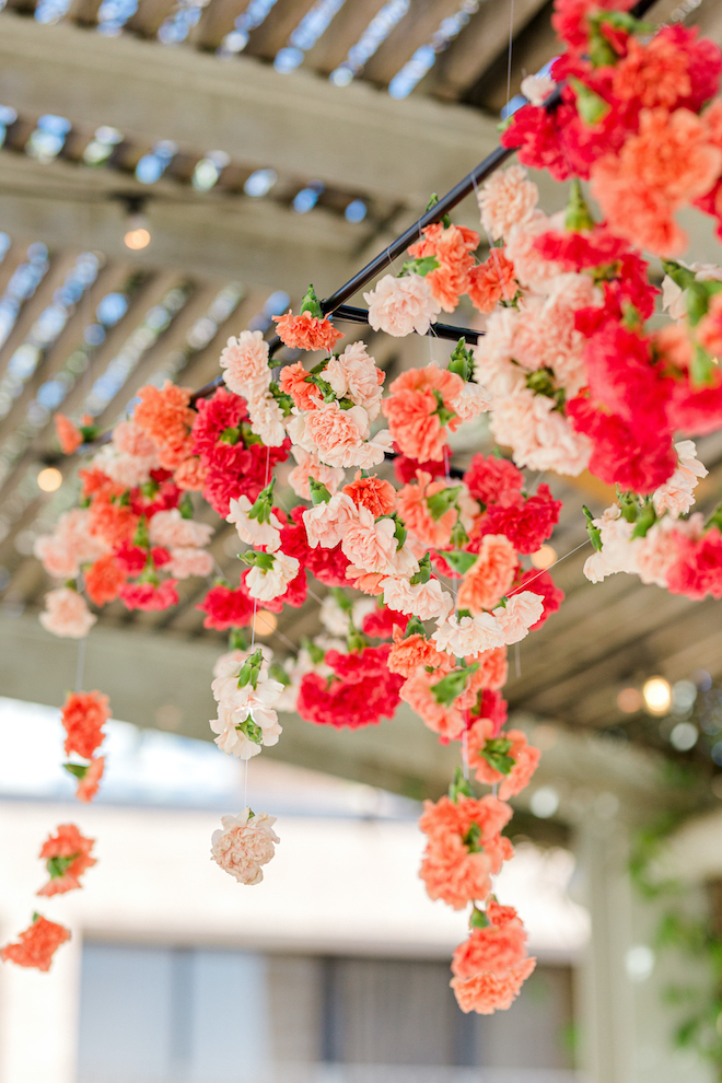 Red, orange and blush flowers hanging over the reception tables at the alfresco celebration.