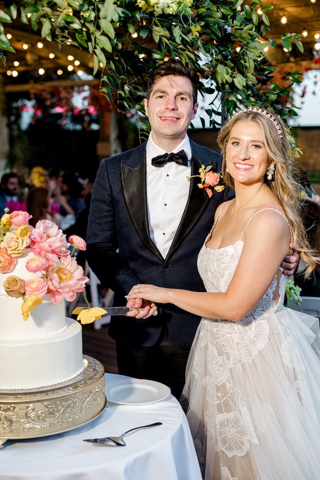 The bride and groom smiling as they cut their cake with bright florals by Susie's Cakes. 