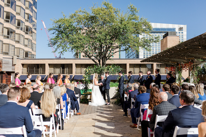 The bride and groom holding hands at their alfresco ceremony at the Four Seasons Hotel Houston.