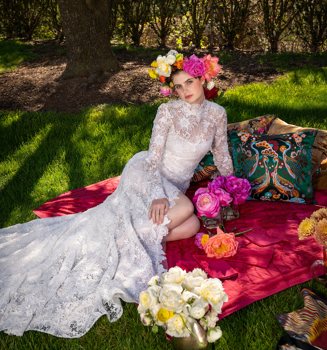 Lace bridal gown being worn by a model with a flower crown on sitting in the grass.