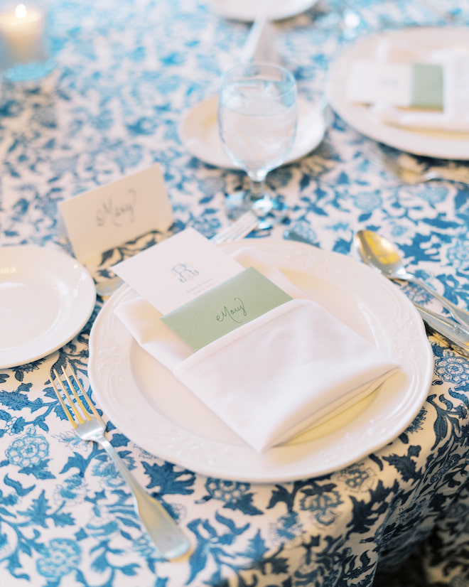 A white table setting with a green hand-written note on a blue floral tablecloth.