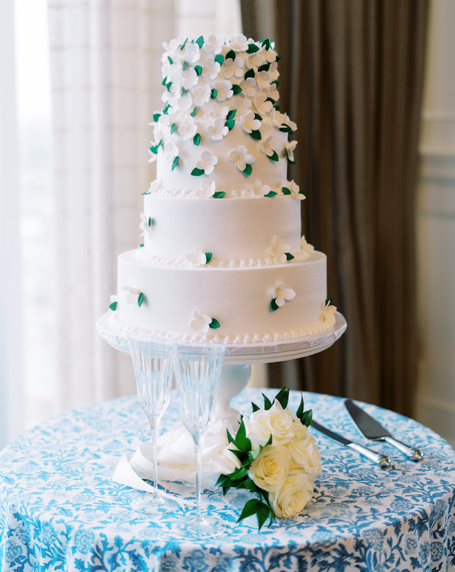 Four-tiered wedding cakes with white and green floral appliques on a floral print tablecloth.
