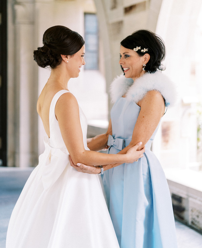 The bride and her mother holding arms and smiling at eachother.