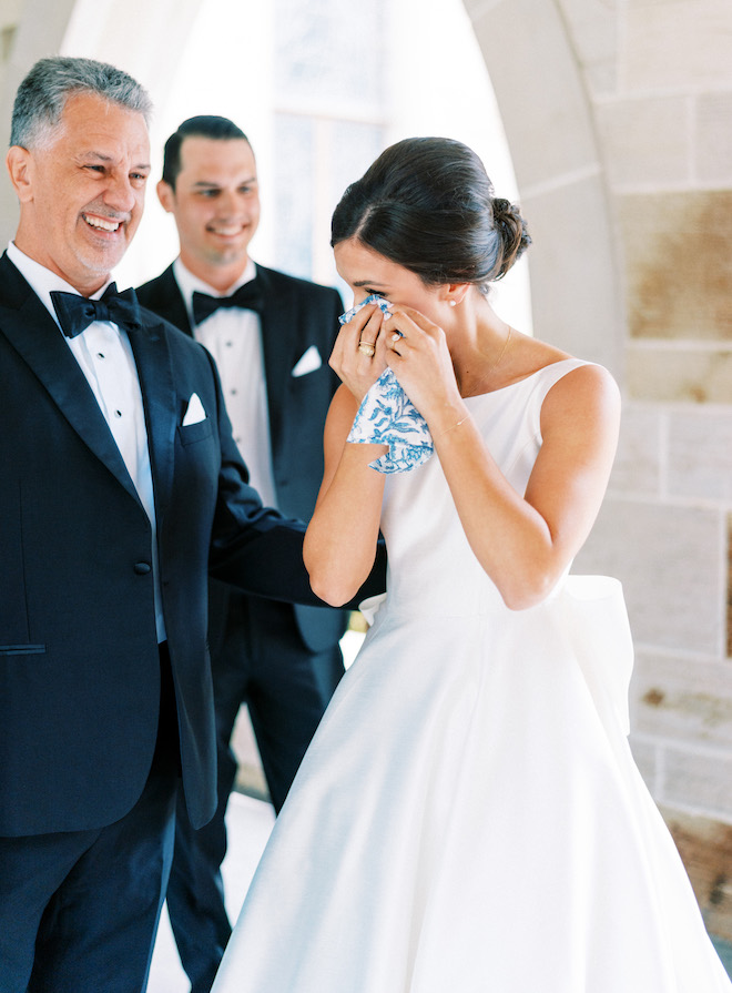 The bride wiping a tear with a floral handkerchief after seeing her dad.