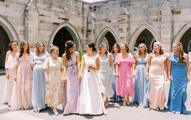The bride walking with her bridesmaids while wearing colorful gowns.
