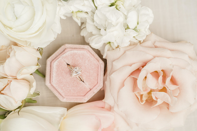The brides wedding ring resting in a blush pink velvet box with white and blush roses surrounding it.